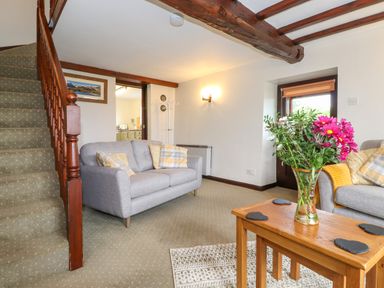 A living room with two grey sofas a wooden coffee table with flowers and a staircase at Addylea Cottage in Cartmel Fell near Windermere