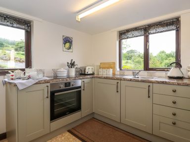A kitchen with oven sink toaster kettle and kitchen utensils by windows at Addylea Cottage in Cartmel Fell near Windermere