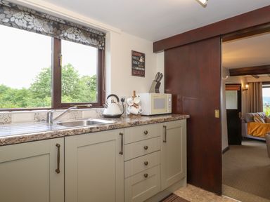 A kitchen with a sink microwave kettle and knife block next to a sliding wooden door at Addylea Cottage in Cartmel Fell near Windermere