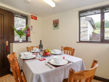 A dining room with a set table featuring bowls glasses and a bottle with flowers on a windowsill at Addylea Cottage in Cartmel Fell near Windermere