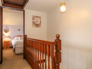 A hallway with a wooden railing leading to a bedroom with a bed and nightstand at Addylea Cottage in Cartmel Fell near Windermere