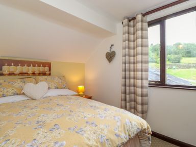 A bedroom with a bed covered in yellow floral bedding next to a window with plaid curtains at Addylea Cottage in Cartmel Fell near Windermere