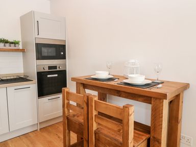 A kitchen with wooden table and chairs set with bowls and glasses next to a microwave and oven at Pear Tree Cottage in St Mellion near St Dominick