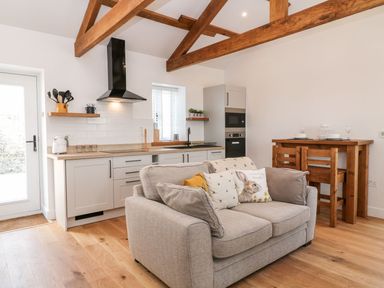 A kitchen with white cabinets wooden countertops and a beige sofa with animal print pillows at Pear Tree Cottage in St Mellion near St Dominick