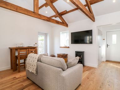 A living room with grey sofa wooden beams wooden floor wall mounted TV and wooden dining table at Pear Tree Cottage in St Mellion near St Dominick