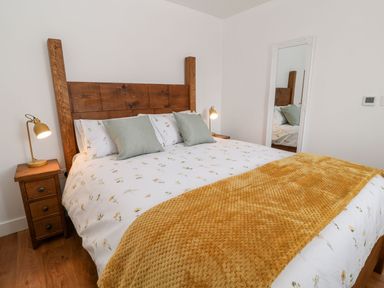 A bedroom with a wooden bed frame two bedside tables with lamps and a full length mirror at Pear Tree Cottage in St Mellion near St Dominick