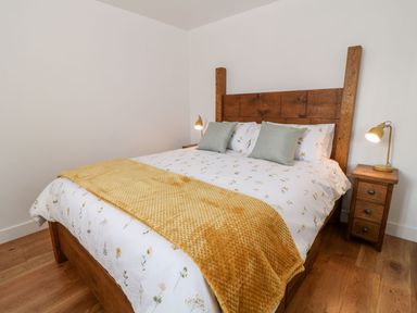 A bedroom with a wooden bed frame two pillows floral bedding yellow blanket wooden floor and nightstand at Pear Tree Cottage in St Mellion near St Dominick