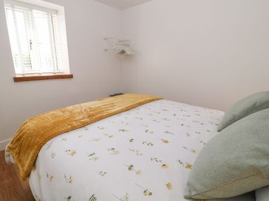 A bedroom with a bed covered in floral bedding and two pillows near a window at Pear Tree Cottage in St Mellion near St Dominick