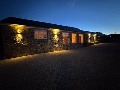 A stone building with exterior lights on and windows glowing at dusk at Old Orchard Barn St Mellion near St Dominick
