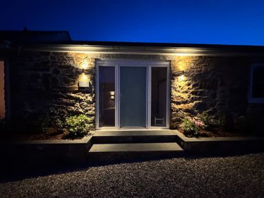 Stone building entrance with glass door and steps lit by wall lights at Old Orchard Barn in St Mellion near St Dominick