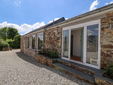 The exterior of a stone building with large windows and an open door on a gravel driveway at Old Orchard Barn St Mellion near St Dominick