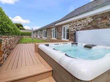 An outdoor deck with a hot tub and a lawn area beside a stone building at Old Orchard Barn St Mellion near St Dominick
