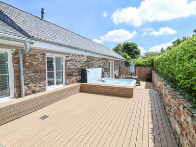 An outdoor deck with a hot tub dining table chairs umbrella and stone wall at Old Orchard Barn St Mellion near St Dominick