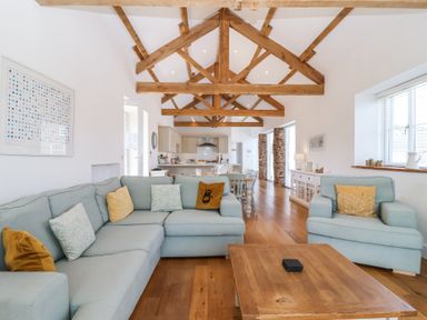 An open living area with light blue sofas yellow and patterned cushions and exposed wooden ceiling beams at Old Orchard Barn St Mellion near St Dominick