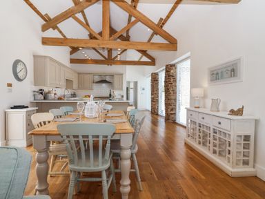 A kitchen and dining area with wooden beams and a wooden dining table at Old Orchard Barn in St Mellion near St Dominick