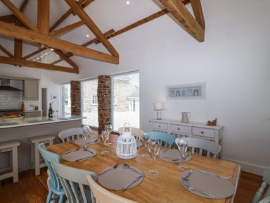A dining area with a wooden table set with placemats and glassware in a room with exposed wooden beams at Old Orchard Barn St Mellion near St Dominick