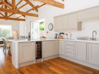 A kitchen with wooden beams beige cabinets white countertops and a dining table with chairs at Old Orchard Barn St Mellion near St Dominick