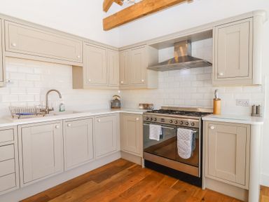 A kitchen with beige cabinets stainless steel stove white subway tile backsplash and wooden floor at Old Orchard Barn St Mellion near St Dominick