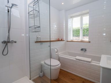 A bathroom with a bathtub a toilet a shower and a window with blinds at Old Orchard Barn St Mellion near St Dominick