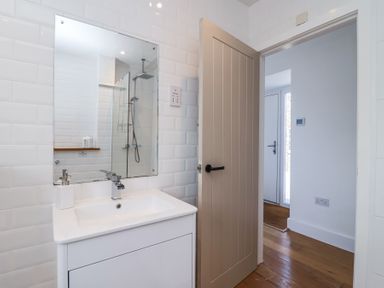 A bathroom with a sink and mirror next to an open door showing a hallway at Old Orchard Barn in St Mellion near St Dominick