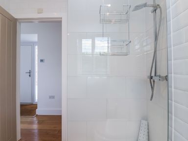 A bathroom shower area with a wall-mounted showerhead and a metal hanging shower caddy at Old Orchard Barn St Mellion near St Dominick