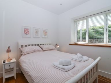 A bedroom with a double bed with striped bedding white towels on the bed a nightstand with a lamp and a window with blinds at Old Orchard Barn St Mellion near St Dominick