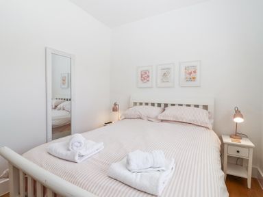 A bedroom with a bed with striped bedding towels on the bed two bedside tables with lamps and a full length mirror on the wall at Old Orchard Barn in St Mellion near St Dominick