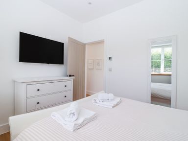 A bedroom with a bed, a chest of drawers, a wall-mounted TV, a wall mirror, and an open door at Old Orchard Barn St Mellion near St Dominick