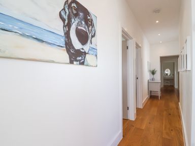 A hallway with wooden floor a painting of a dog on the wall and a small table with a plant at Old Orchard Barn St Mellion near St Dominick