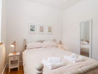 A bedroom with a double bed striped bedding bedside tables with lamps three framed flower pictures above the bed and a standing mirror at Old Orchard Barn St Mellion near St Dominick