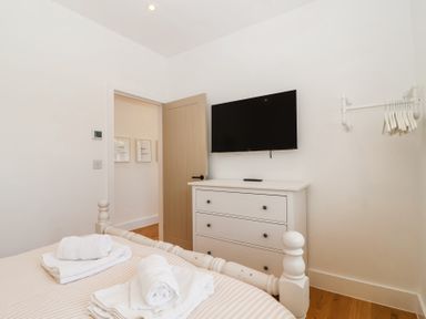 A bedroom with a bed holding folded towels a white dresser with a mounted television and a clothing rack at Old Orchard Barn St Mellion near St Dominick