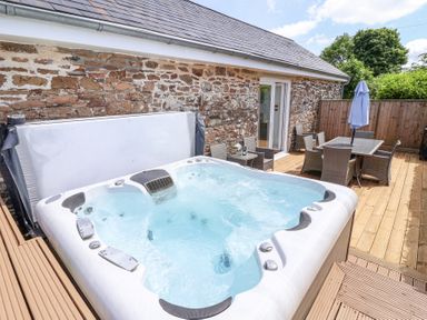 An outdoor patio with a hot tub wooden decking and a dining table with chairs at Old Orchard Barn St Mellion near St Dominick