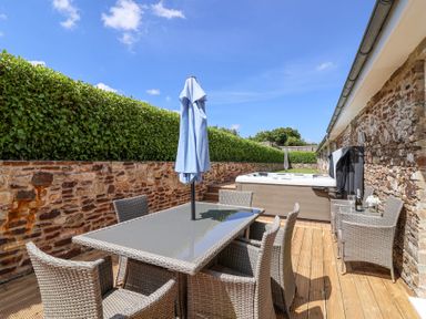 An outdoor patio with a dining table set and a hot tub next to a stone wall at Old Orchard Barn St Mellion near St Dominick