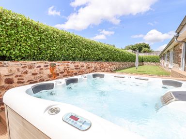 An outdoor hot tub in a garden next to a stone wall and hedge at Old Orchard Barn St Mellion near St Dominick