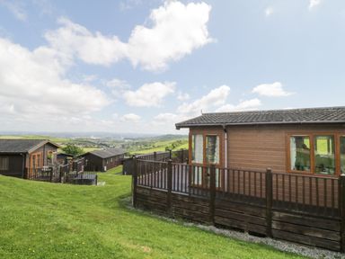 Wooden holiday lodges on a grassy hillside with a view over countryside and distant town at Lodge 16 Whitsand Bay near Millbrook