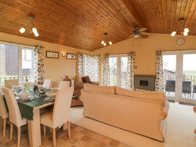 A combined dining and living room with a wooden ceiling and large windows at Lodge 16 in Whitsand Bay near Millbrook