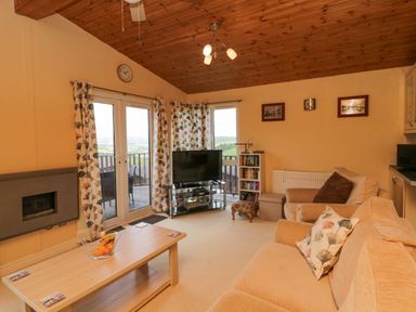 A living room with beige sofas a wooden coffee table and a television near French doors at Lodge 16 in Whitsand Bay near Millbrook