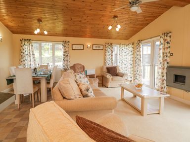 A living room and dining area with beige sofas a coffee table dining table and floral curtains at Lodge 16 Whitsand Bay near Millbrook