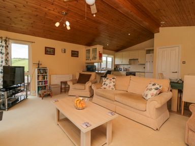 A living room with beige sofas a coffee table with fruit a television and an open kitchen at Lodge 16 Whitsand Bay near Millbrook