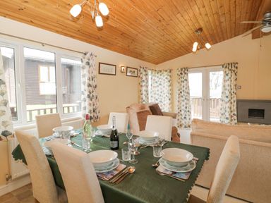 A dining table set with dishes and glasses next to a living area with sofas and floral curtains at Lodge 16 Whitsand Bay near Millbrook