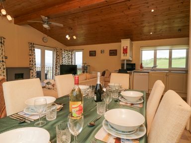 A dining table set with bowls glasses and cutlery in an open plan kitchen and living room with wooden ceiling at Lodge 16 in Whitsand Bay near Millbrook