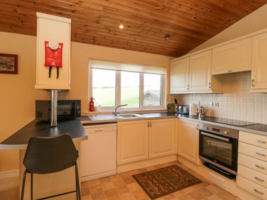 A kitchen with white cabinets a black countertop a window a dishwasher a microwave oven and a chair at Lodge 16 in Whitsand Bay near Millbrook