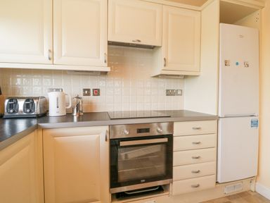 A kitchen with white cabinets a black countertop a built in oven a white refrigerator a toaster a kettle and a coffee pot at Lodge 16 in Whitsand Bay near Millbrook