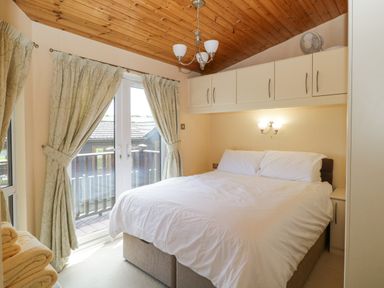 A bedroom with a double bed white bedding overhead cabinets and curtains by glass doors at Lodge 16 Whitsand Bay near Millbrook