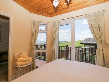 A bedroom with a bed and folded towels on a chair next to windows and a door leading to a balcony at Lodge 16 Whitsand Bay near Millbrook