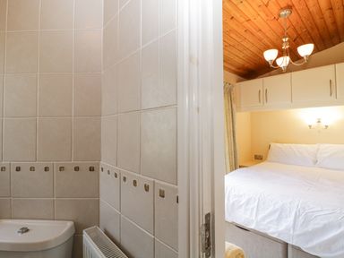 A bathroom with tiled walls and a toilet next to a bedroom with a bed under cabinets and a wooden ceiling at Lodge 16 Whitsand Bay near Millbrook