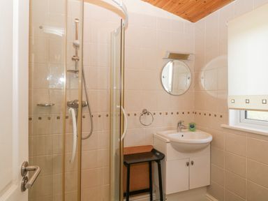 A bathroom with a shower enclosure a sink with cabinet a round mirror and a window at Lodge 16 Whitsand Bay near Millbrook