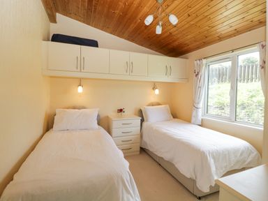 A bedroom with two single beds a chest of drawers and a window at Lodge 16 in Whitsand Bay near Millbrook
