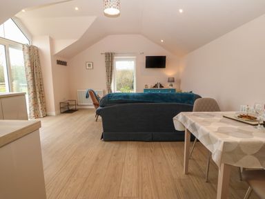 A living room with a sofa facing a wall mounted television and a table with chairs at Y Felin in Caernarfon