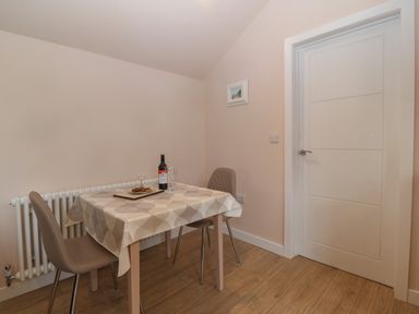 A dining area with a table covered by a tablecloth two chairs a bottle of wine and glasses next to a white door at Y Felin in Caernarfon